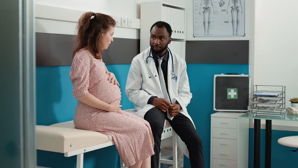 Pregnant woman sitting on an examination bed talking with her doctor