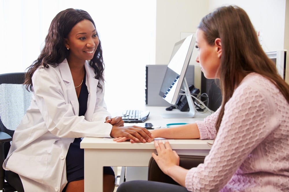 Doctor holding a patient’s hand reassuringly across her consulting desk