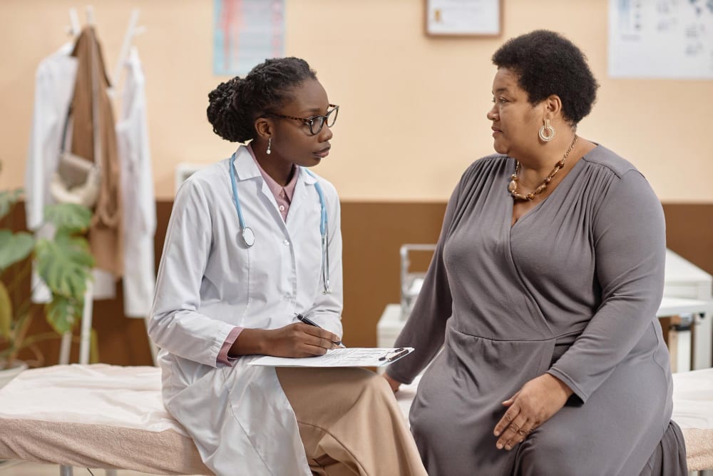 Doctor taking notes while talking with an older woman in a consulting room