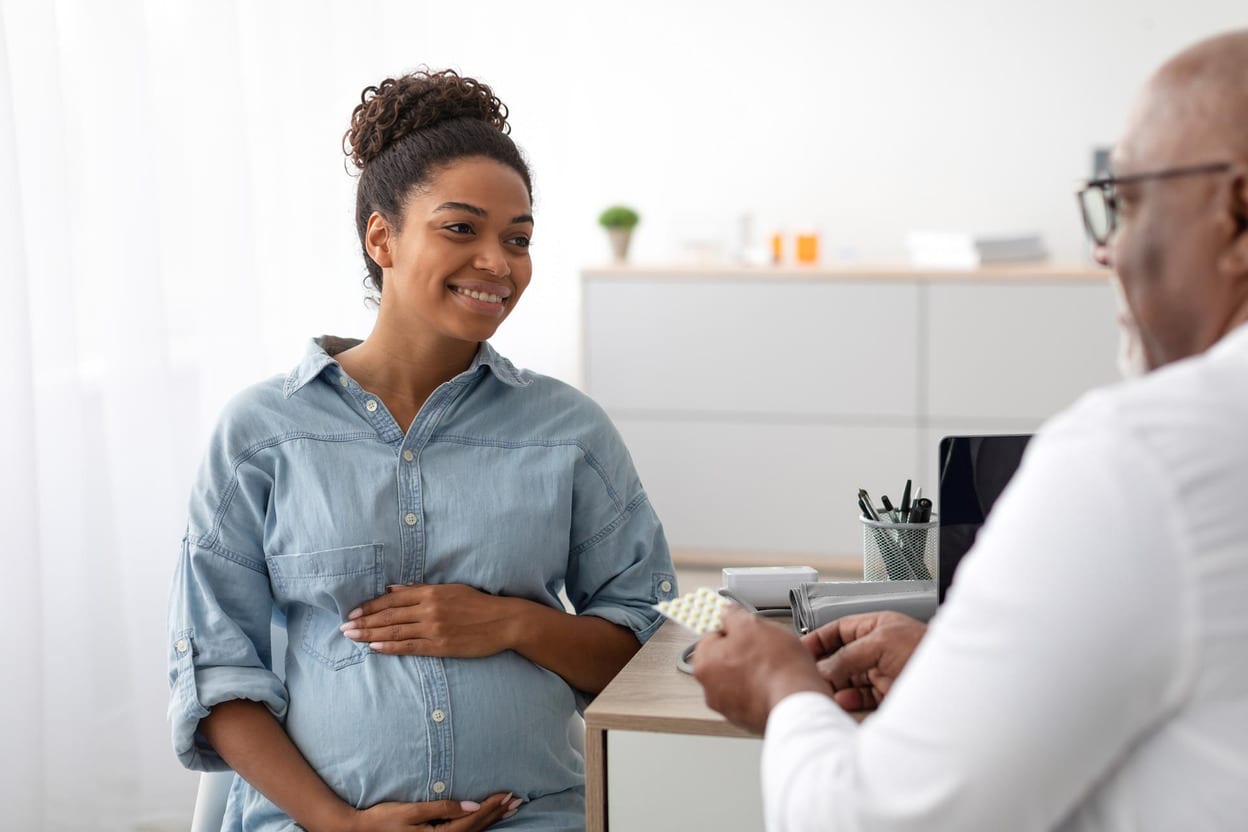 Smiling pregnant woman in a denim shirt talking with her doctor during a consultation