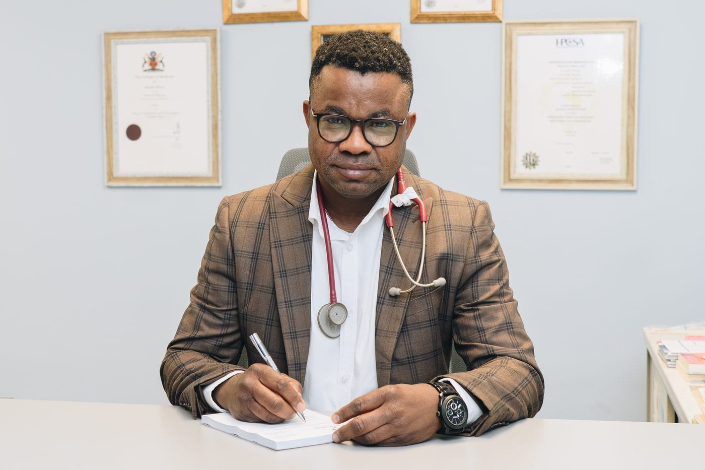Dr Malonda Makanda writing notes at his desk in his consulting room
